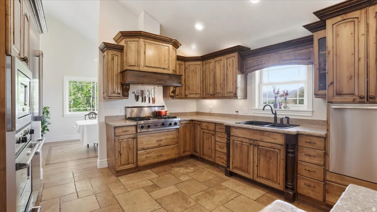 Spacious kitchen featuring custom wood cabinetry, stone-finish countertops, stainless steel appliances, a gas range with an integrated hood, and large format tile flooring