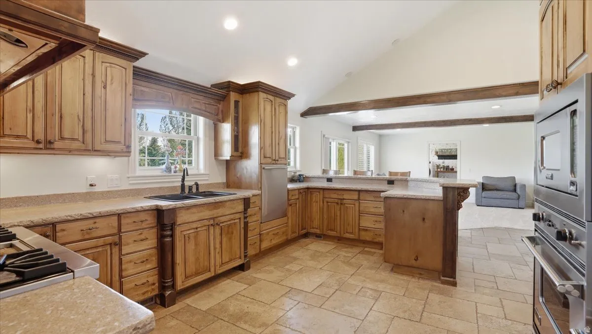Spacious kitchen featuring warm wood cabinetry, neutral stone countertops, a double basin sink, and integrated stainless steel appliances