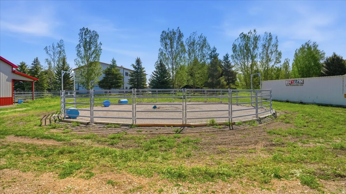 Circular metal fence structure with a gravel interior, surrounded by grass and mature trees