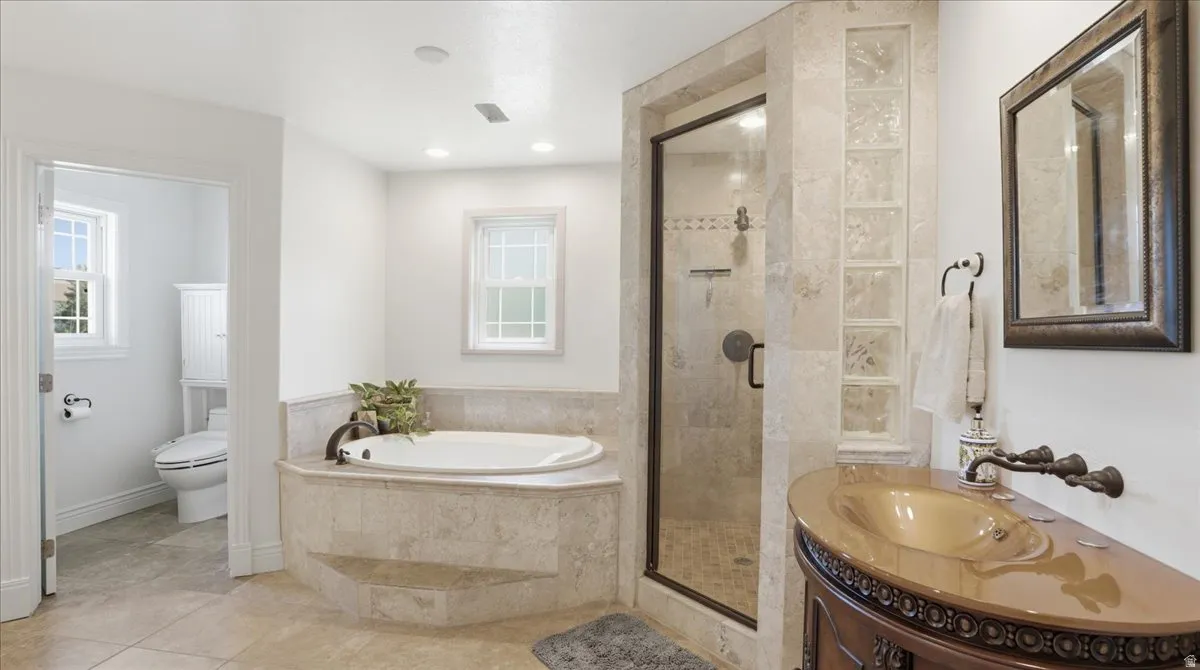 Spa-like bathroom featuring a jetted soaking tub, tiled shower with glass enclosure, single vanity with vessel sink, and an enclosed water closet
