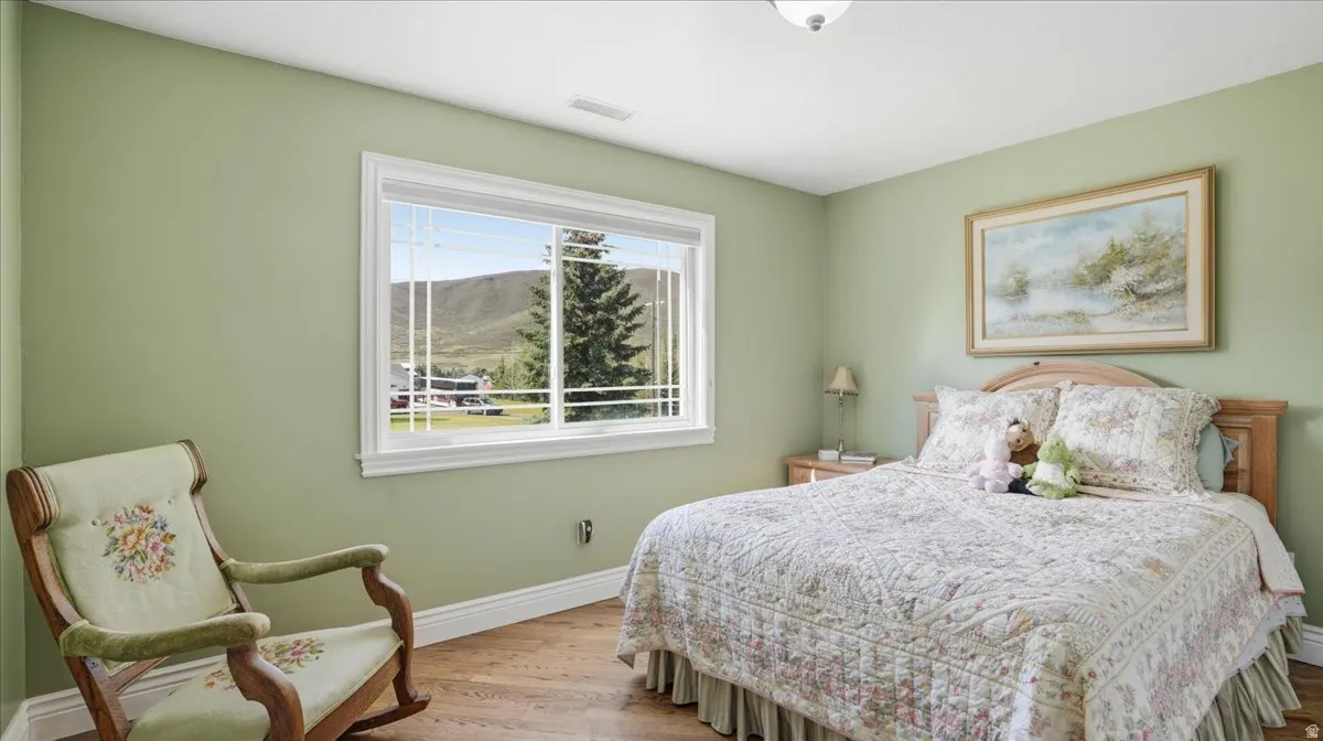 Bedroom featuring light green walls, wood-finish flooring, and white baseboards