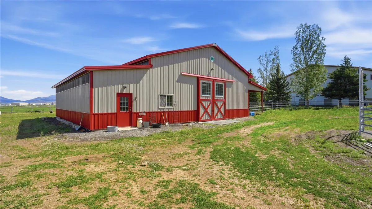 Metal utility building featuring a red trim, red double barn doors, a single red entry door, and multiple windows