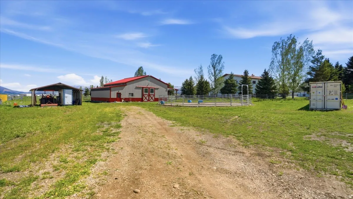 Expansive grounds featuring a gravel driveway, a large barn with red trim, a covered open-air structure, and a round pen