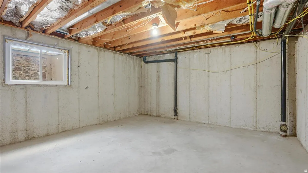 Unfinished basement featuring exposed wood joists, concrete flooring, and a single window