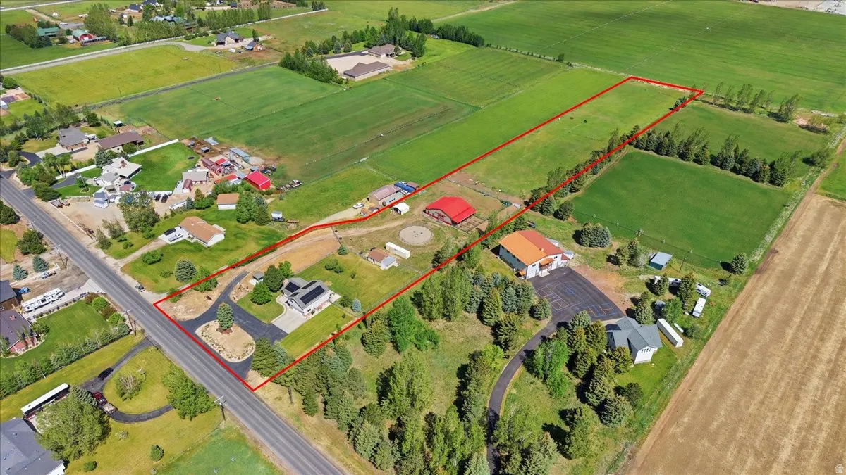 Expansive agricultural property featuring multiple structures, paved driveways, a large red barn, and extensive green fields