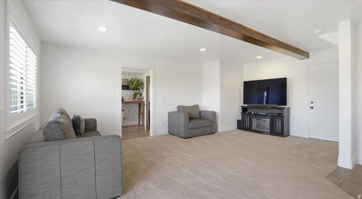 Spacious living area featuring neutral carpeting, recessed lighting, and a prominent wood-finish beam