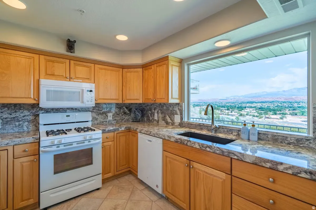 Kitchen featuring light wood cabinetry, stone-finish countertops, a white gas range with an over-the-range microwave, and a large window providing expansive panoramic scenery