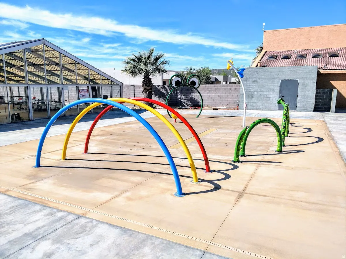 Dedicated splash pad featuring colorful arched water features, a frog-themed sprayer, and a caterpillar-themed water arch
