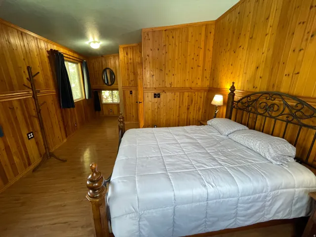 Bedroom featuring extensive wood paneling, wood-finish flooring, multiple windows, built-in cabinetry, and a ceiling-mounted light fixture
