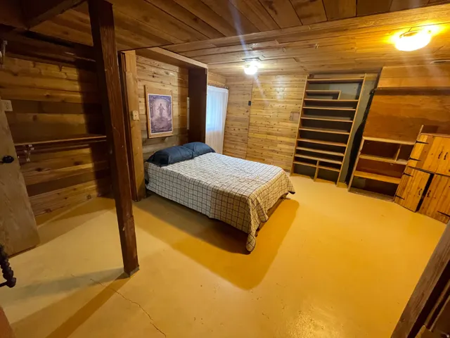 Wood-paneled room featuring wood-finish walls and ceiling, painted concrete flooring, an open closet with shelving and hanging rod, and built-in shelving units