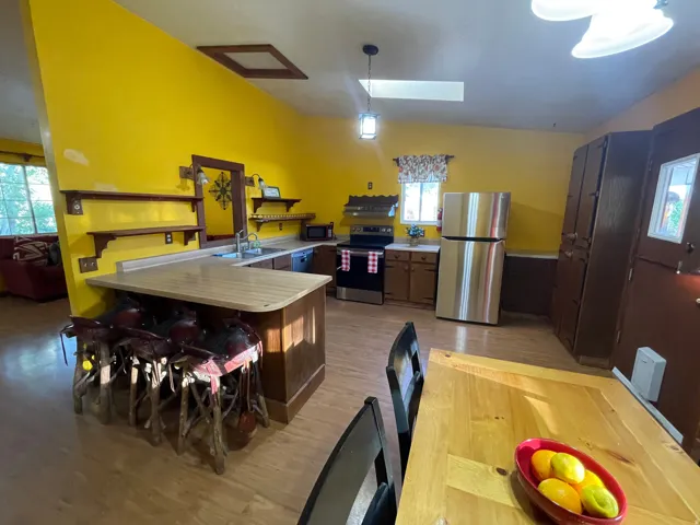Kitchen featuring wood-finish flooring, a U-shaped countertop with a breakfast bar, stainless steel refrigerator and range, and multiple built-in storage cabinets
