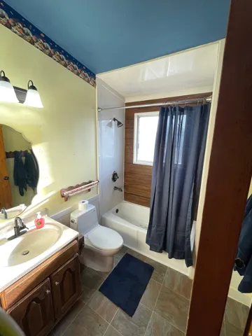 Bathroom featuring a wood-finish vanity with an integrated sink, a white toilet, and a combined tub and shower with wood-panel detailing