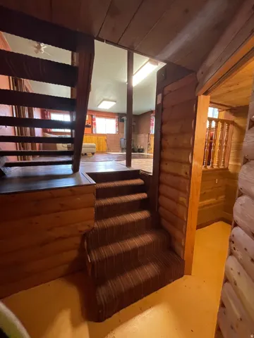 Carpeted staircase with wood-paneled walls and exposed log accents