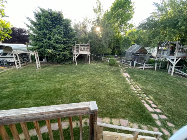 Expansive green lawn featuring multiple raised play structures, mature trees, and a stone-paver pathway
