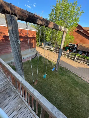 Wood-plank balcony overlooking a green lawn with a rustic timber swing set