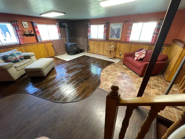Lower level recreation space featuring wood-finish flooring, brick accent wall, and a wood-burning stove