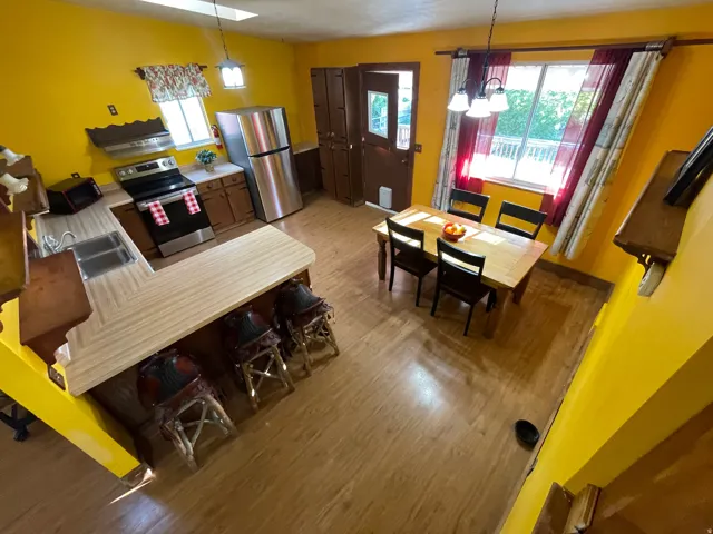 Open-concept kitchen and dining area featuring wood-finish flooring, L-shaped countertop with integrated sink, stainless steel appliances, and a dining space with a window