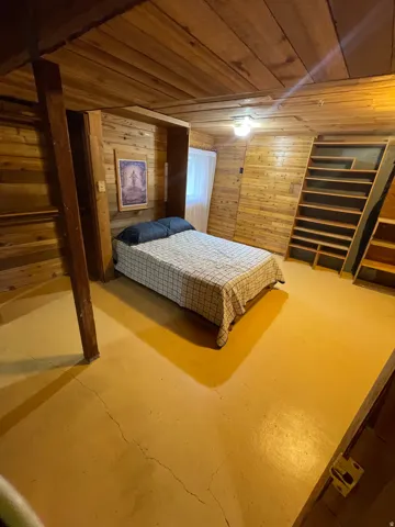 Room featuring comprehensive wood-paneling on walls and ceiling, painted concrete flooring, and built-in shelving
