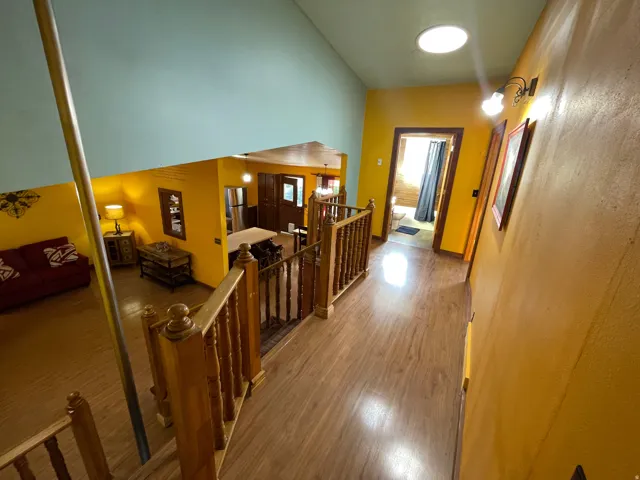 Upper-level hallway featuring wood-finish flooring, a skylight, and a light-colored wood balustrade overlooking a lower-level space