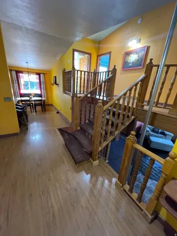 Multi-level interior featuring wood-finish flooring, a wood-spindle staircase with carpeted treads, and a dining area with a chandelier