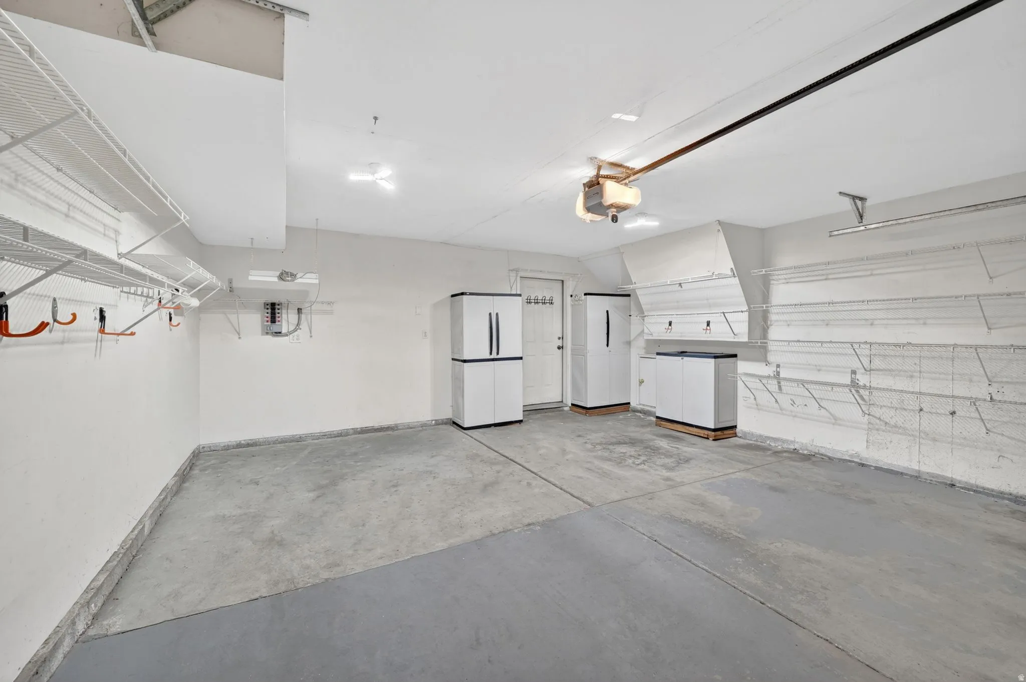 Spacious garage featuring a concrete floor, overhead wire shelving, wall-mounted storage hooks, built-in storage cabinets, and a side access door