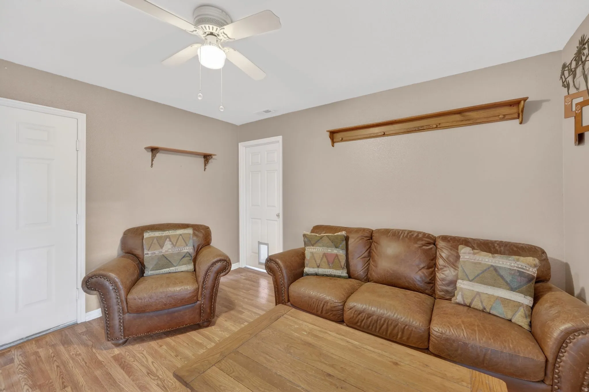 Living area featuring wood-finish flooring, two panel doors, and a ceiling fan with integrated lighting