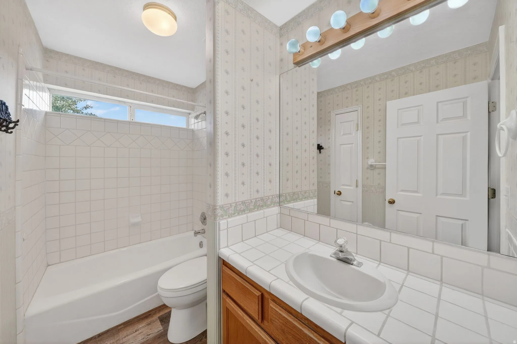 Bathroom featuring a vanity with a drop-in sink, tiled countertop, and a large wall mirror