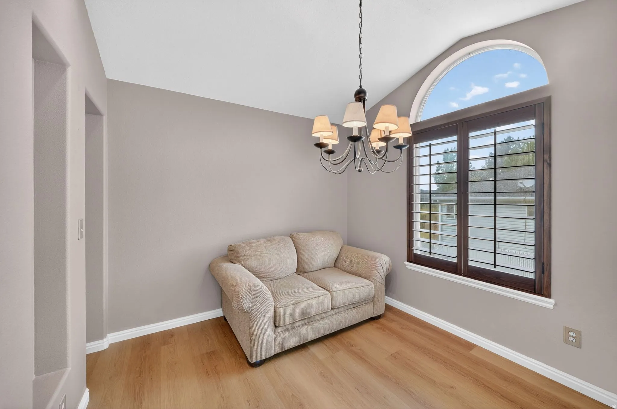 Room featuring wood-finish flooring, a vaulted ceiling, and a prominent arched window with dark wood plantation shutters