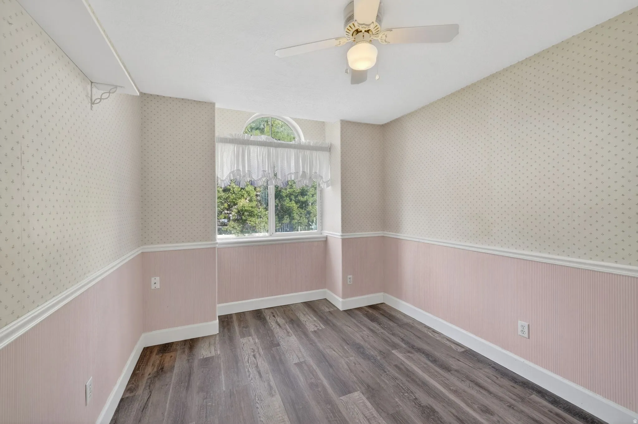 Room featuring wood-finish flooring, a ceiling fan with integrated lighting, and a window with an arched transom