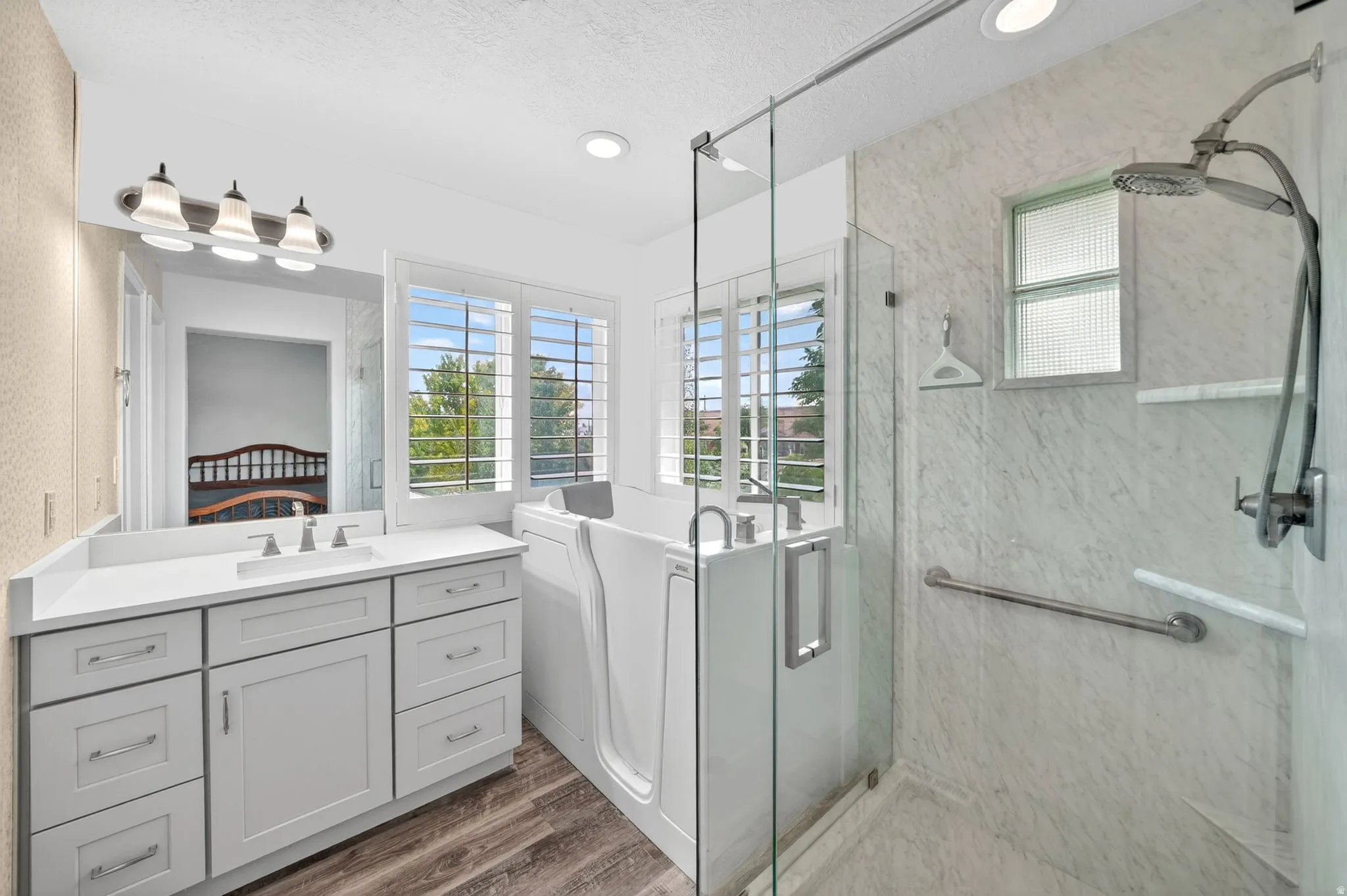 Spacious bathroom featuring a walk-in tub, separate glass-enclosed shower, dual-sink vanity with a quartz countertop, and wood-finish flooring