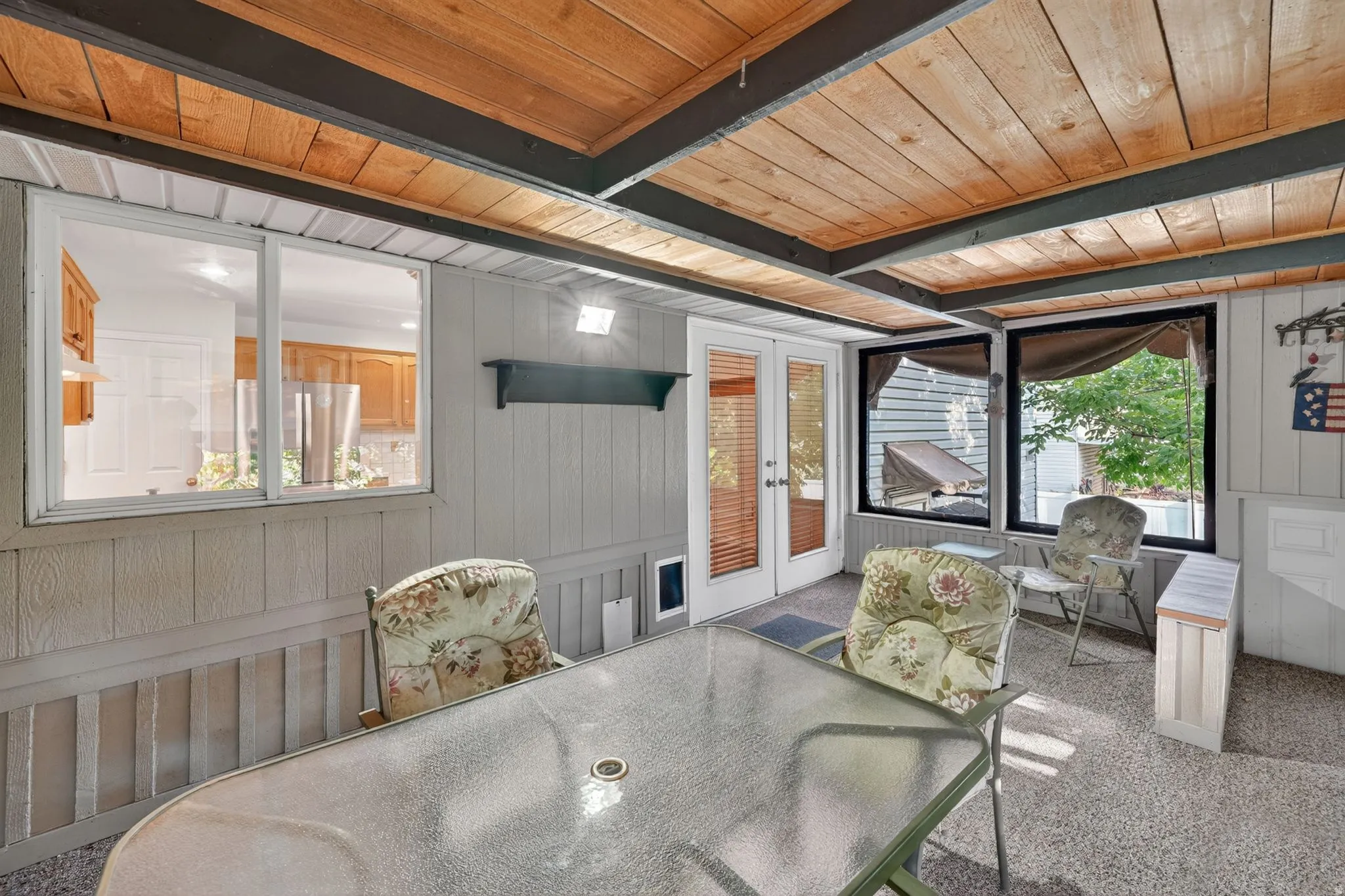 Enclosed porch featuring a wood-panel ceiling with exposed beams, light gray vertical paneling, and a full-light French door entry