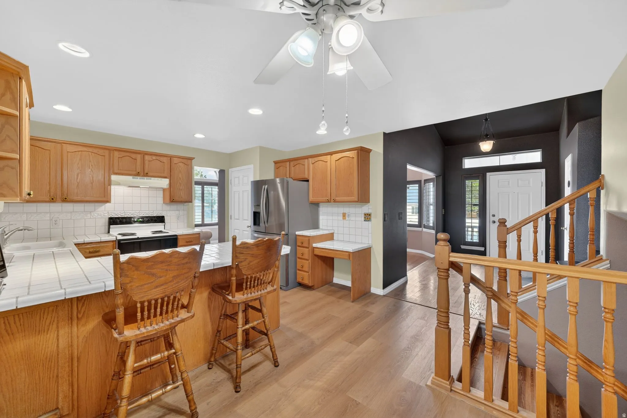 Open-concept kitchen featuring wood-finish flooring, light wood cabinetry, white tile countertops, and a white tile backsplash
