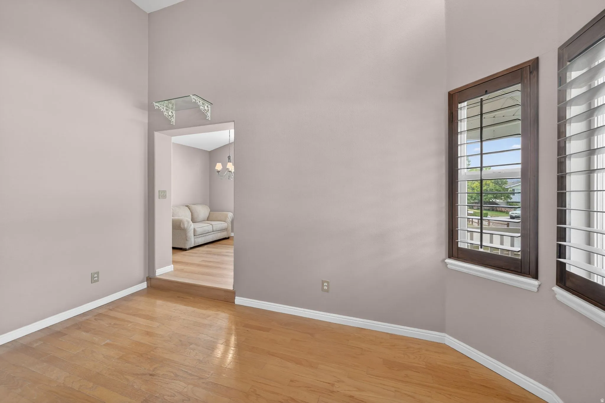 Room featuring natural wood-finish flooring, vaulted ceilings, and a bay window with dark wood framing and plantation shutters
