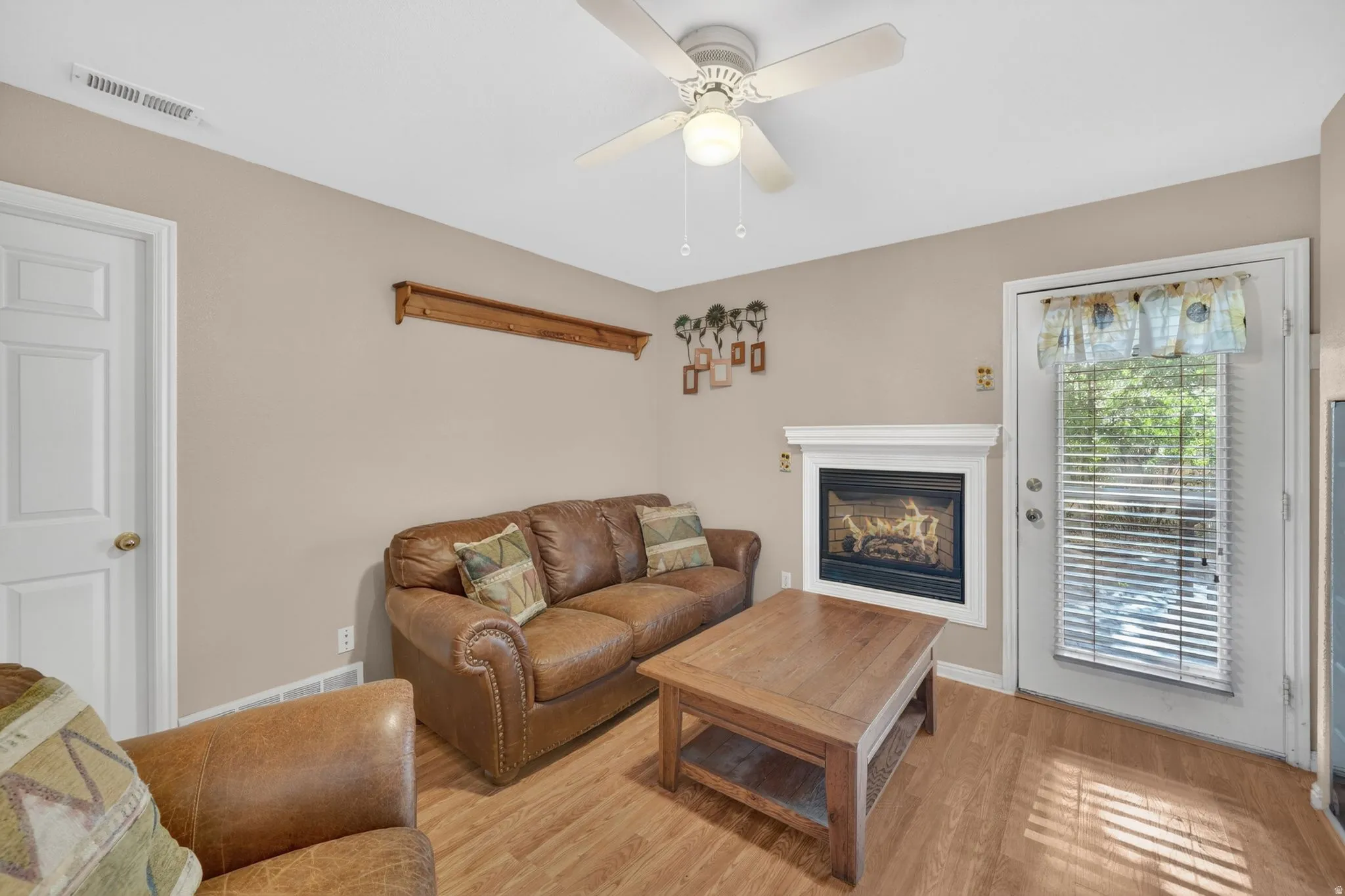 Living area featuring wood-finish flooring, a white-mantled fireplace, and a ceiling fan with integrated lighting