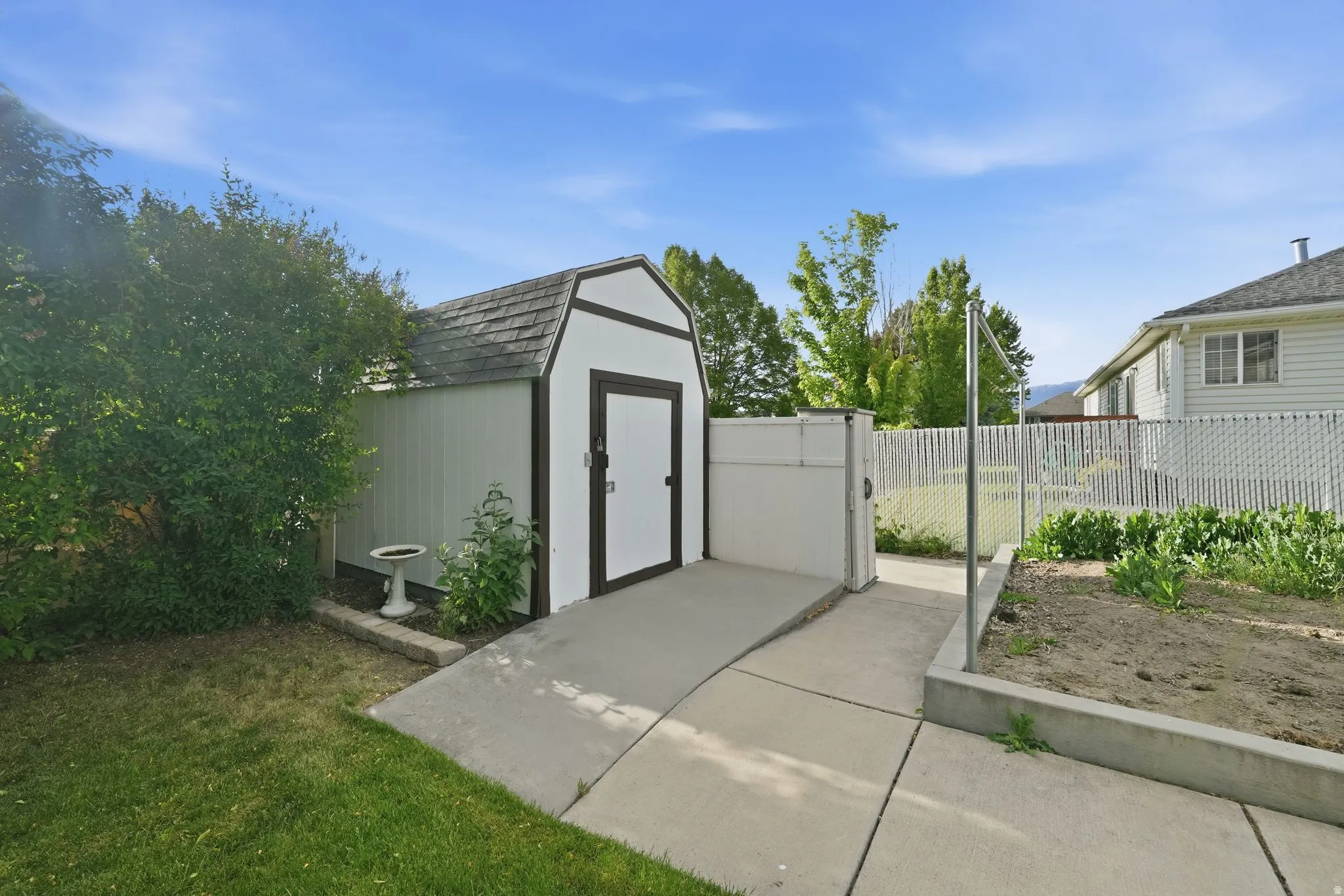 Utility shed with gambrel roof, white siding, and dark trim