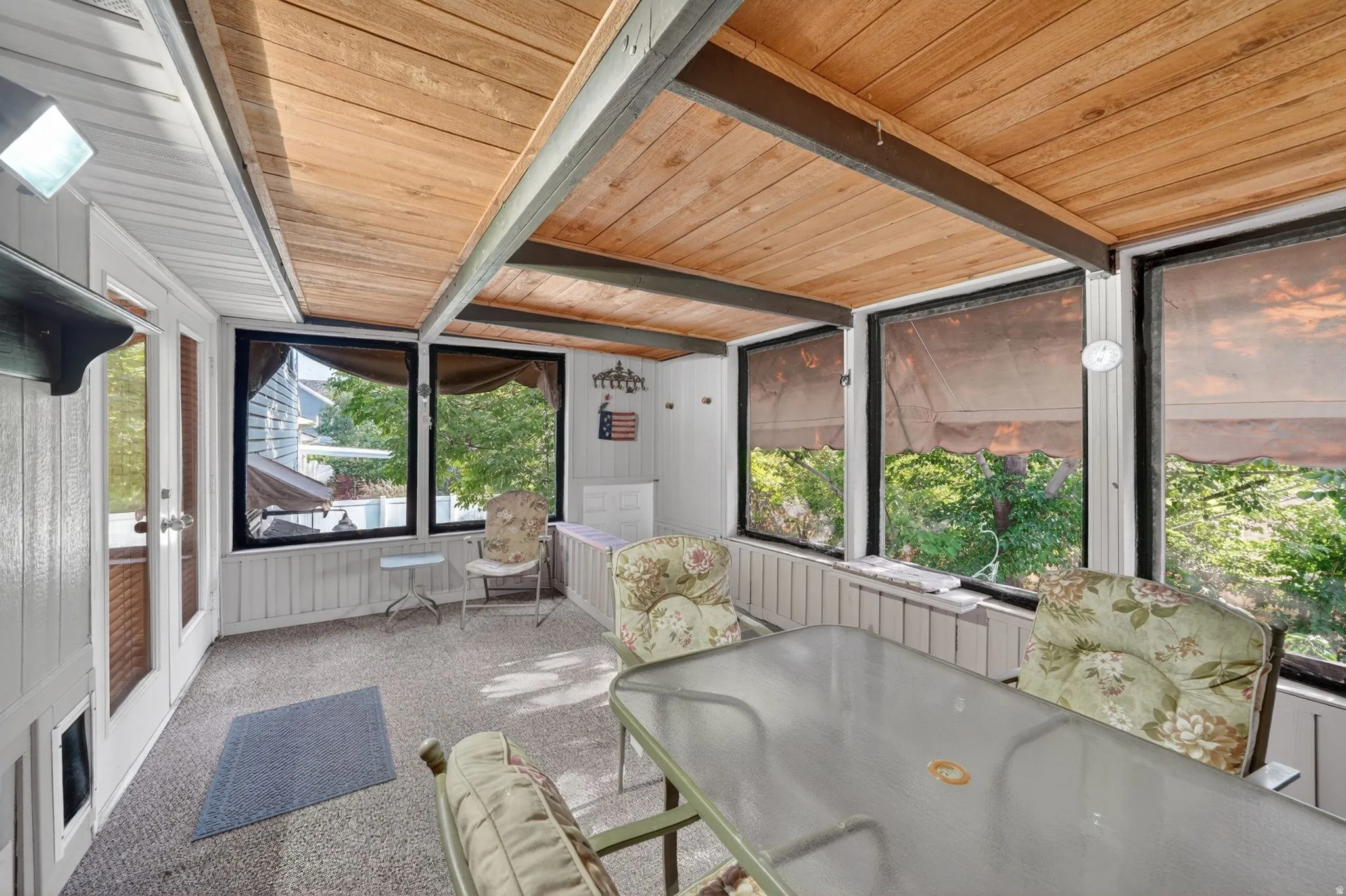 Enclosed porch featuring a wood-panel ceiling with exposed beams, multiple windows, carpet flooring, and white paneled walls