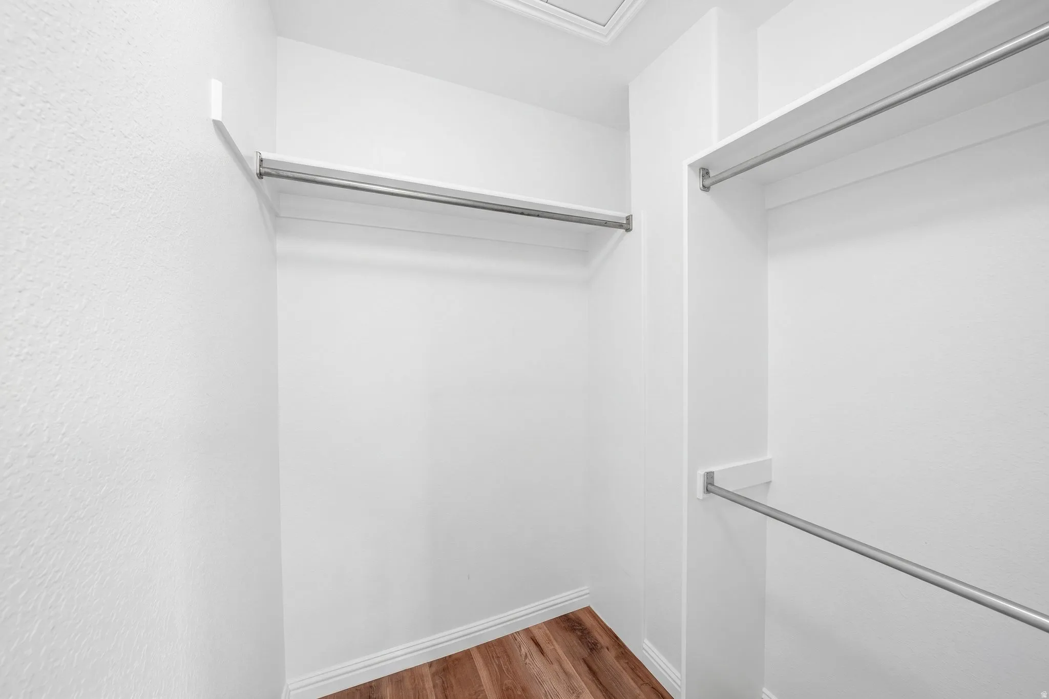 Walk-in closet with multiple white shelving units and metal hanging rods