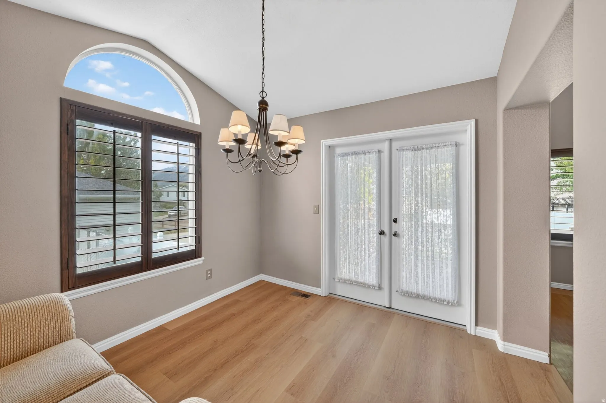 Room with wood-finish flooring featuring a large window with plantation shutters and an arched transom window