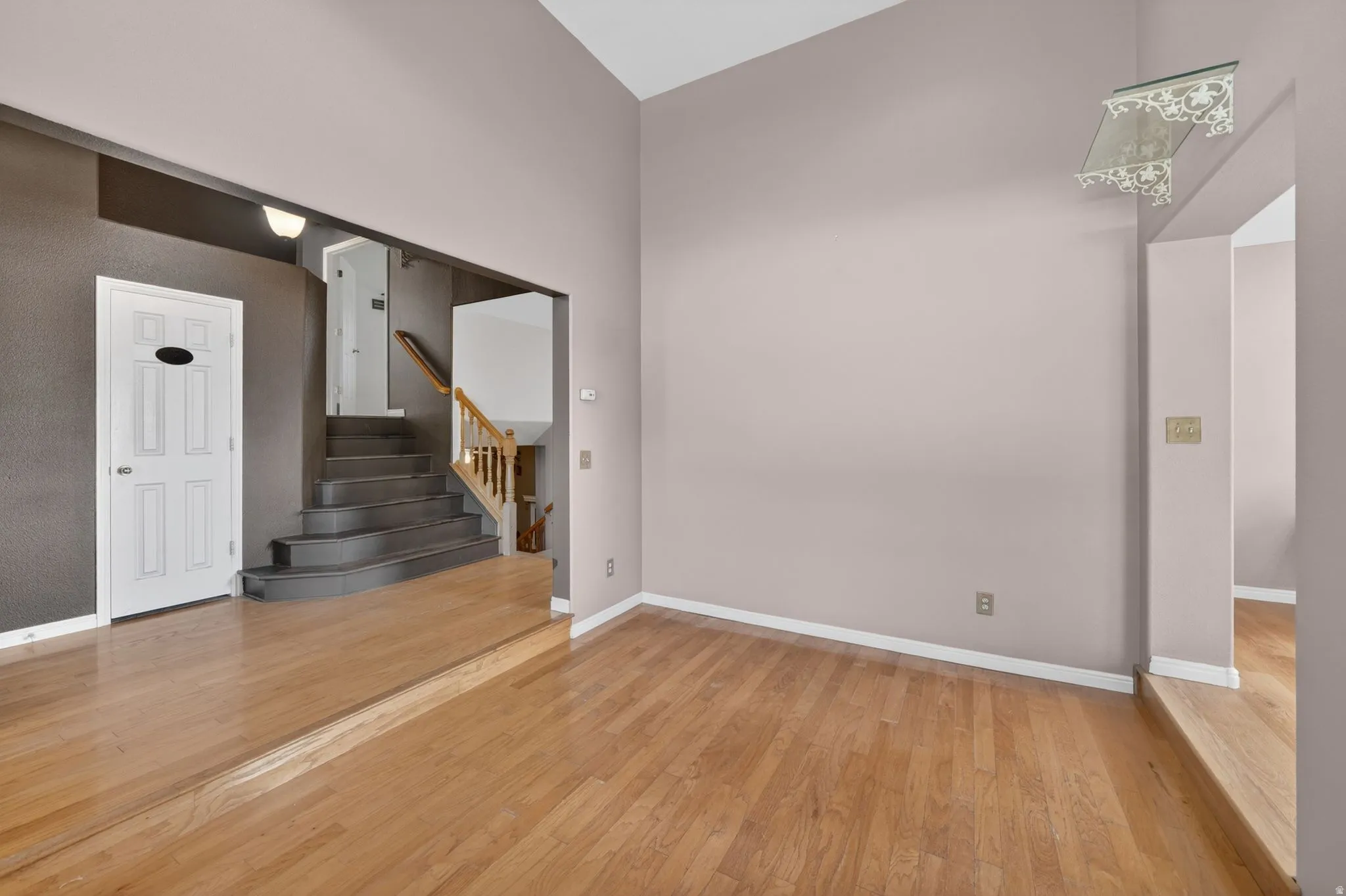 Sunken living area featuring light wood-finish flooring, vaulted ceilings, and a decorative wall shelf