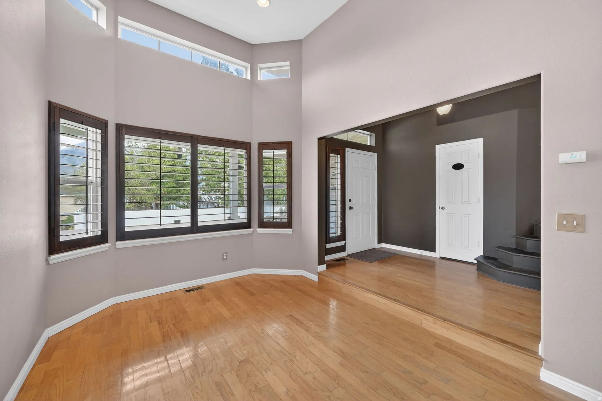 Hardwood-style flooring throughout a sunlit room featuring multiple windows with dark wood frames and white plantation shutters