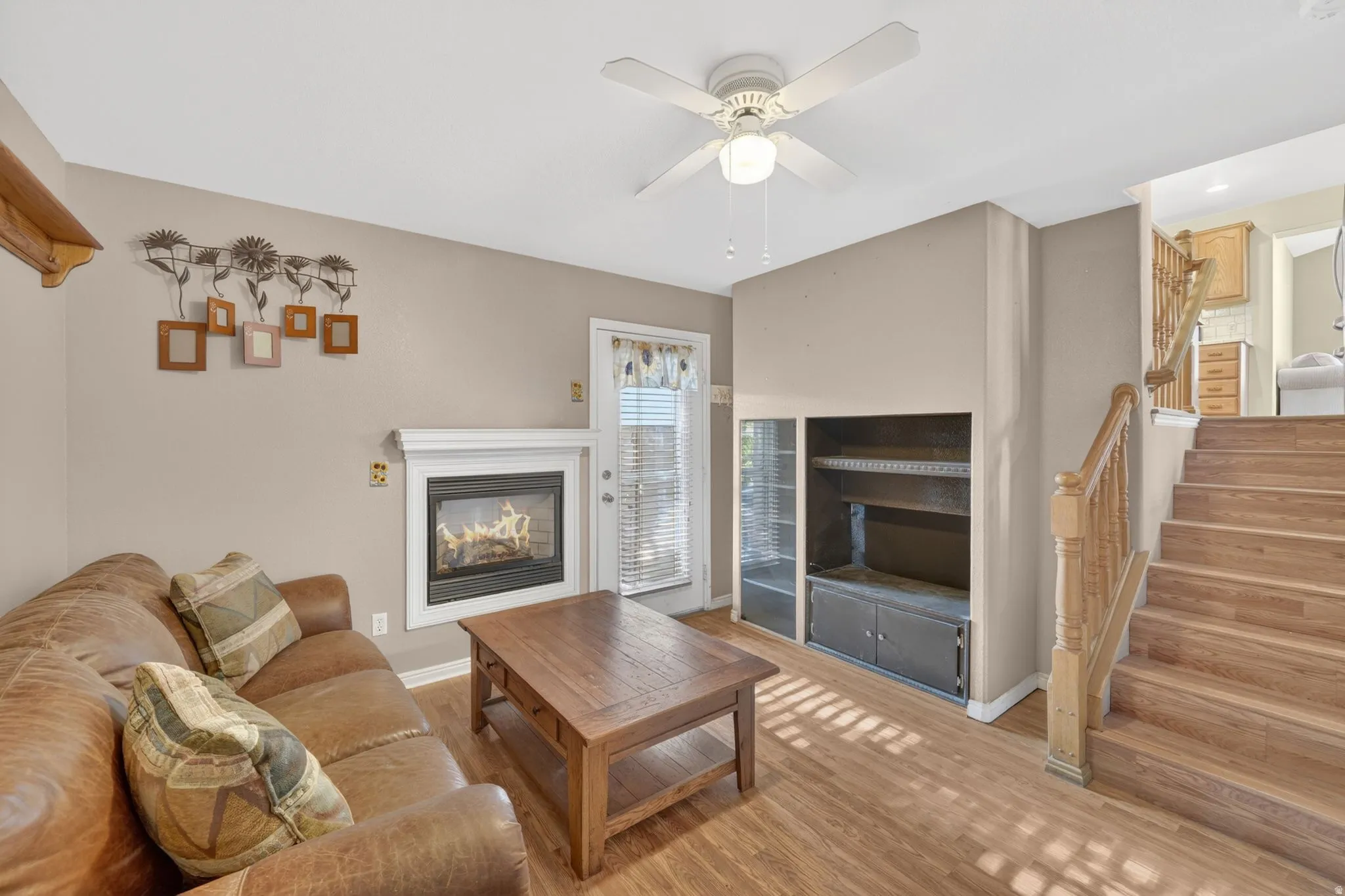Living area featuring wood-finish flooring, a fireplace with a white mantel, and a ceiling fan