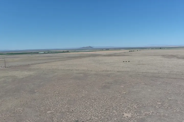 Expansive open land featuring a clear horizon, distant agricultural fields, and natural desert vegetation