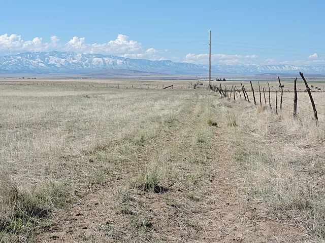 Expansive open field with natural vegetation, defined by a rustic wooden fence line