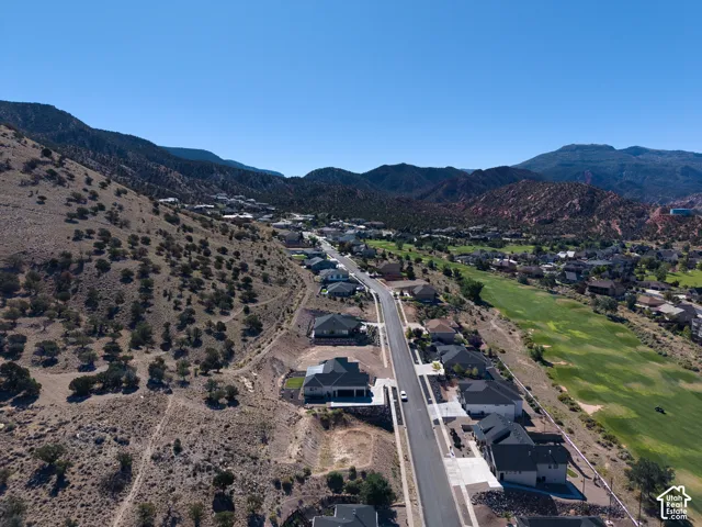 Looking East:  Newly developed residential area with paved streets and contemporary homes, bordering a golf course and natural desert landscape, all set against a backdrop of distant mountains