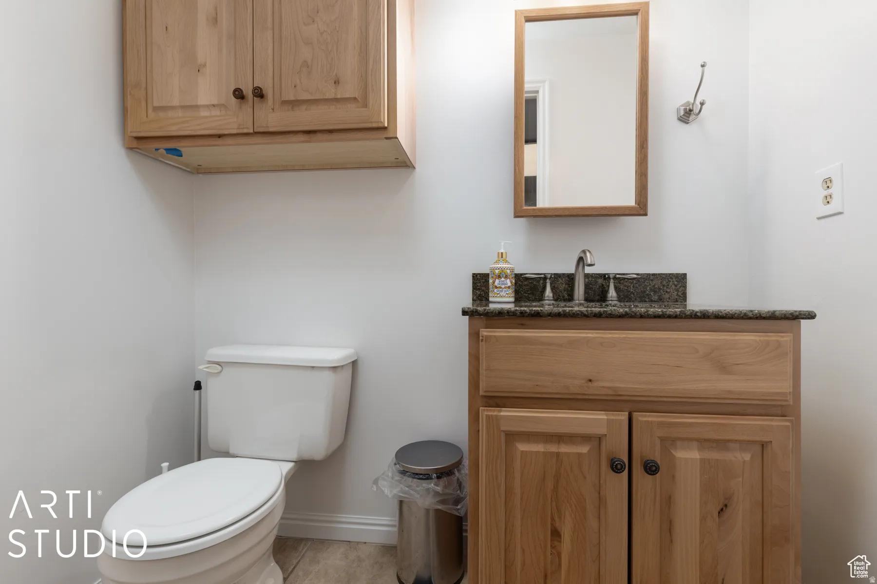Bathroom featuring a wood-finish vanity with a granite-style countertop, a rectangular mirror with a wood-finish frame, and light-toned tile flooring