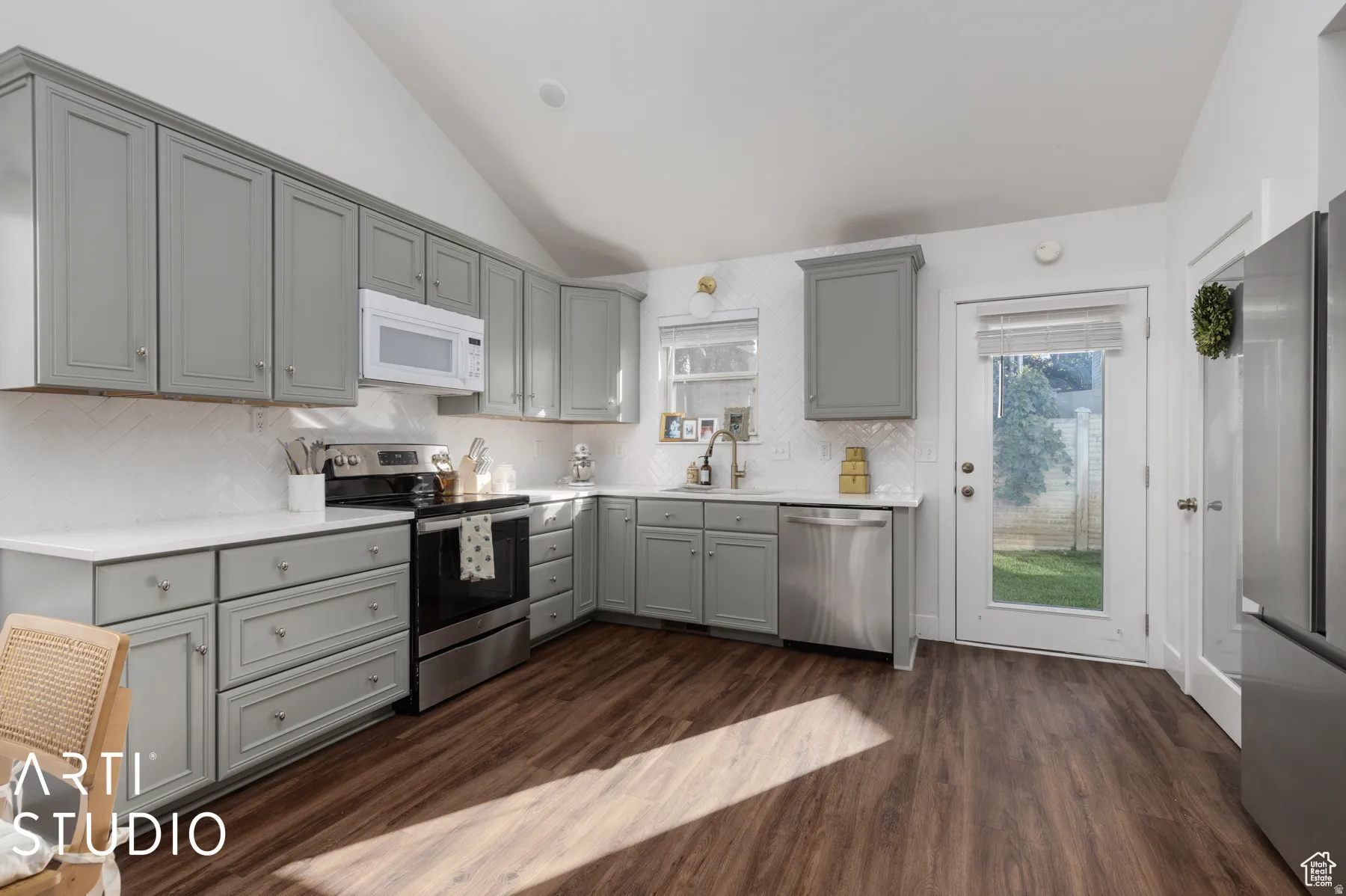 Contemporary kitchen featuring vaulted ceilings, wood-finish flooring, light grey cabinetry, white countertops, and a full suite of stainless steel appliances