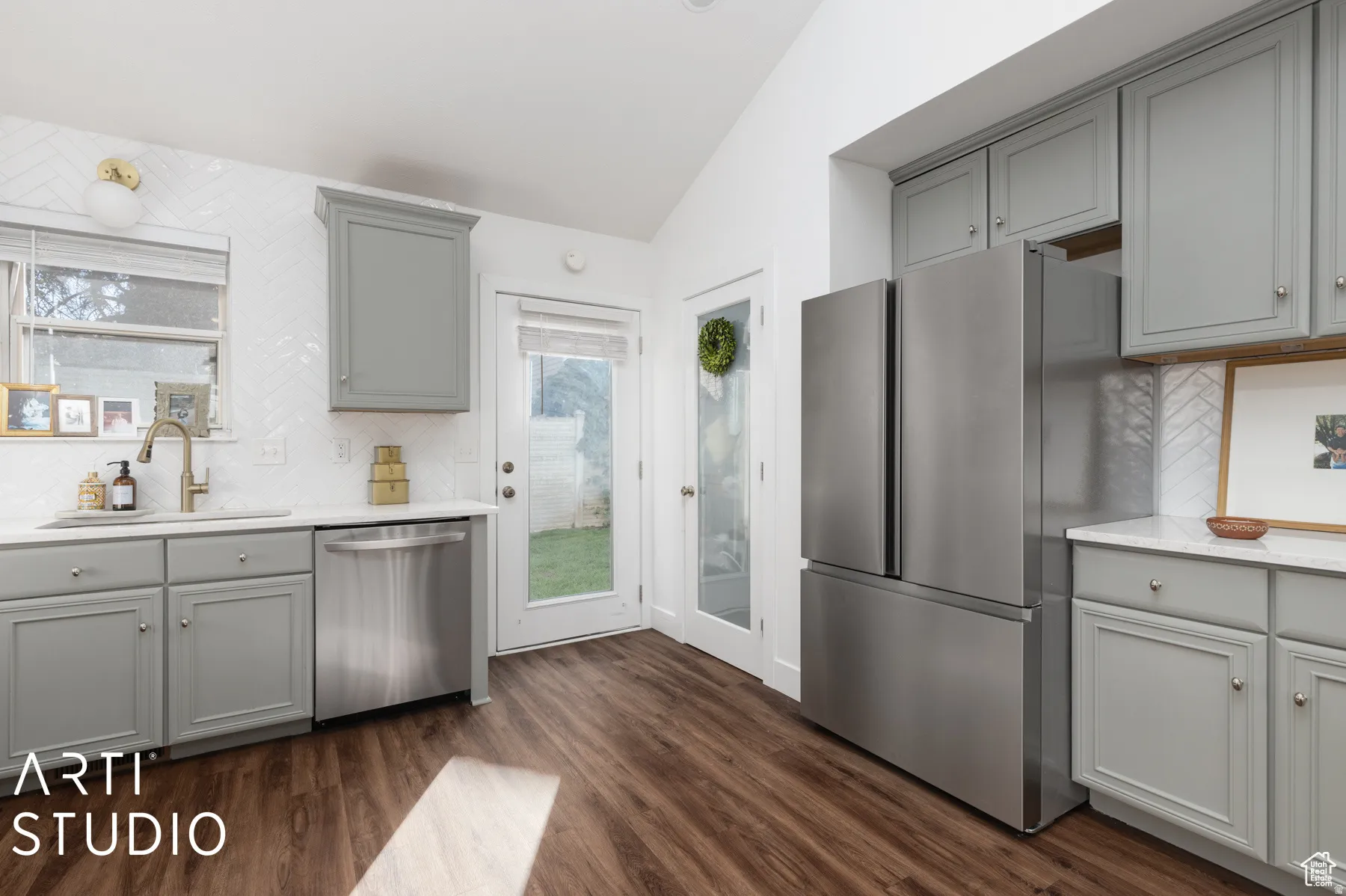 Kitchen featuring wood-finish flooring, gray shaker cabinetry, stainless steel appliances, white countertops, and a white herringbone tile backsplash