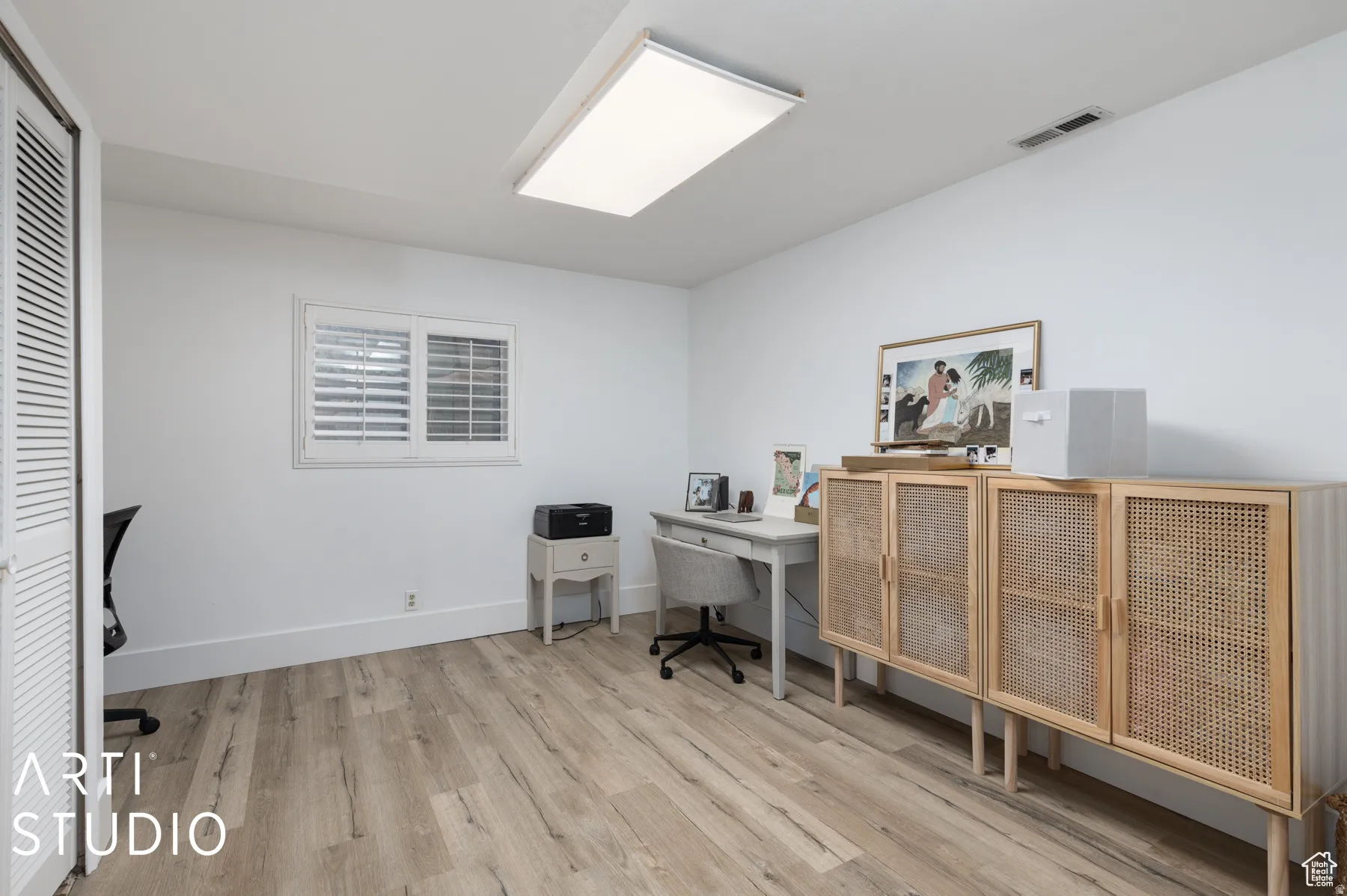 Room featuring wood-finish flooring, white walls, and a window with white louvered shutters
