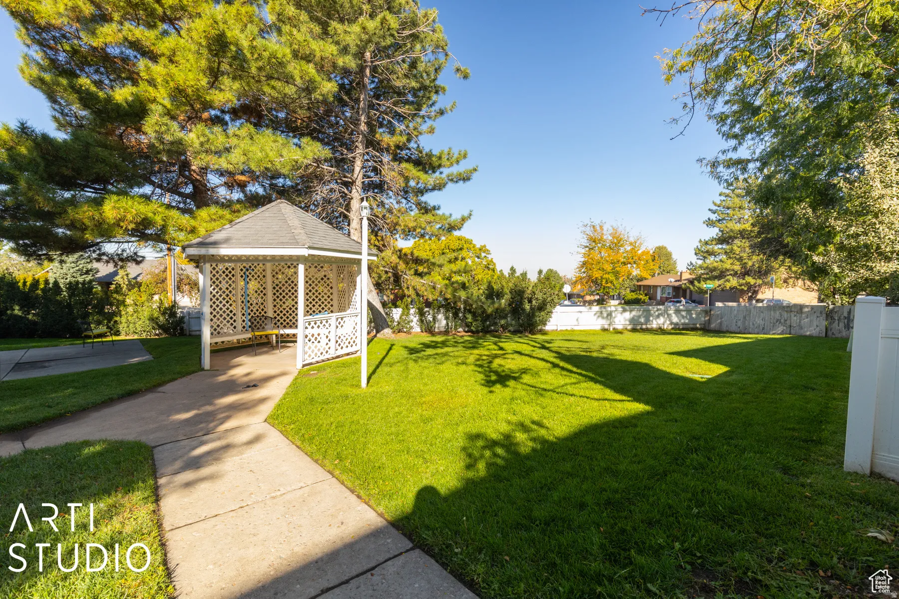 Lattice-paneled gazebo with a shingled roof and built-in seating, set upon a concrete path