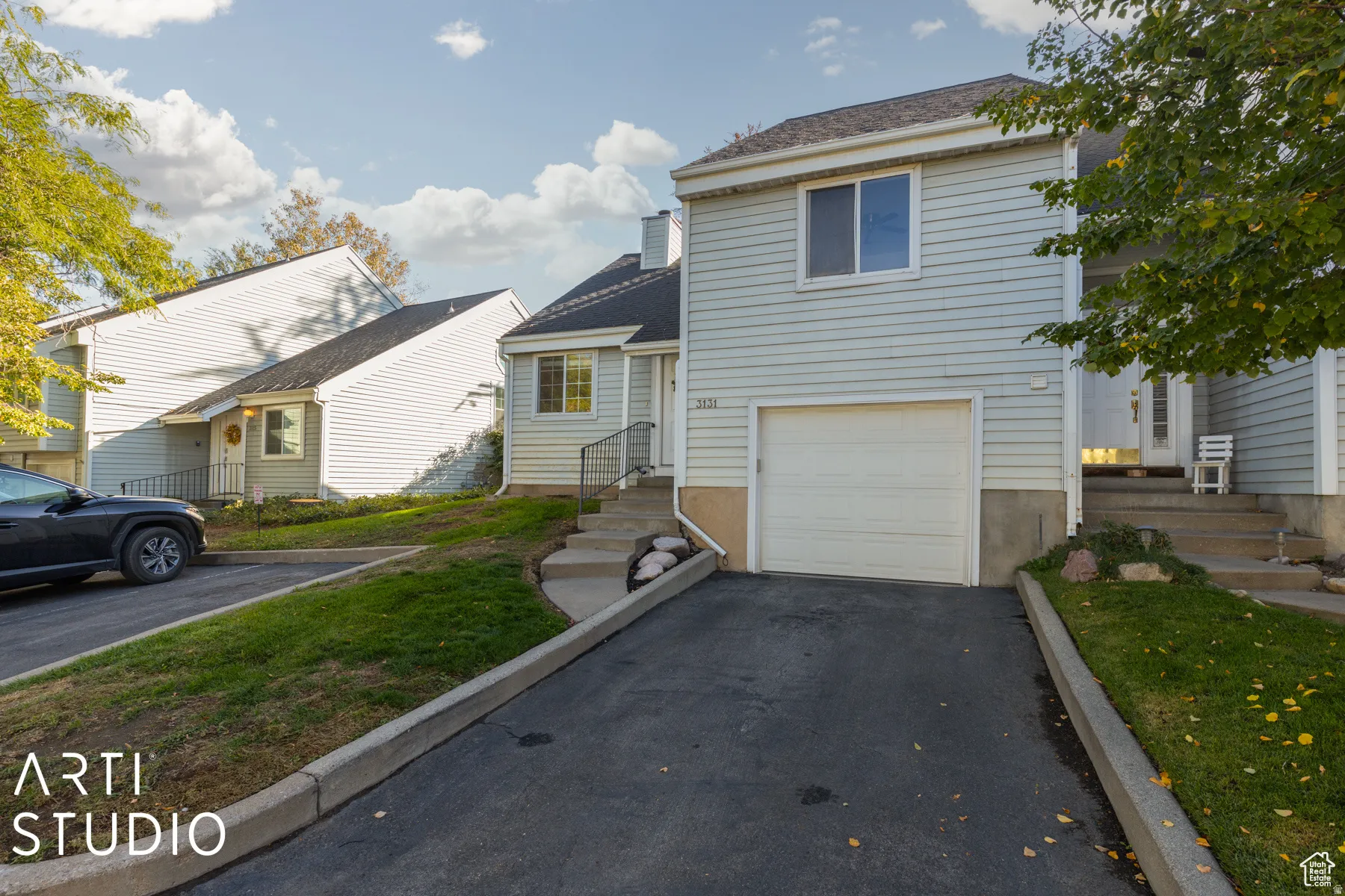 Multi-level townhouse exterior featuring light blue siding, an attached single-car garage, and a paved driveway